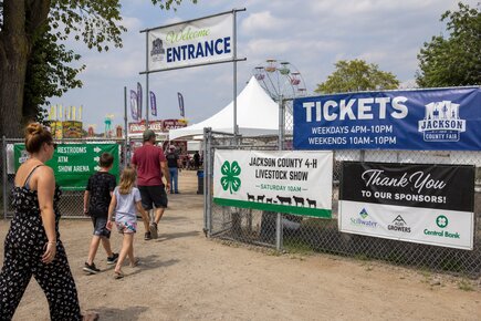 Chain link fence banners at a county fair displaying ticket information 4 h livestock show details sponsors and visitor directions