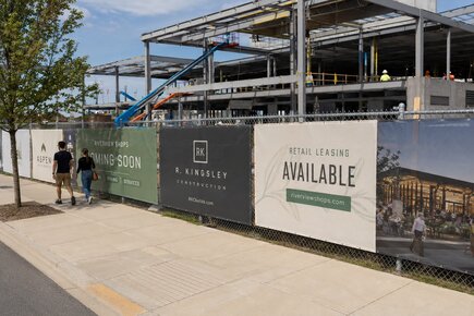 Construction site fence banners along a retail development advertising coming soon stores construction branding and available leasing space
