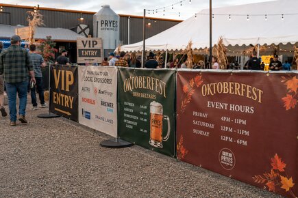 Event fence banners at an oktoberfest entrance displaying vip entry local sponsors beer releases and event hours