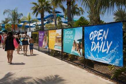 Outdoor fence banners along a water park promoting season passes cabana rentals group events and daily admission