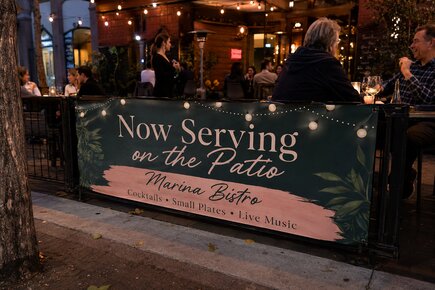 Custom restaurant vinyl banner promoting patio dining at Marina Bistro mounted along an outdoor dining area