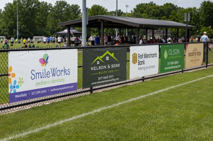 Custom fence banners for baseball stadium displaying business sponsors along a chain link fence around the sports field perimeter