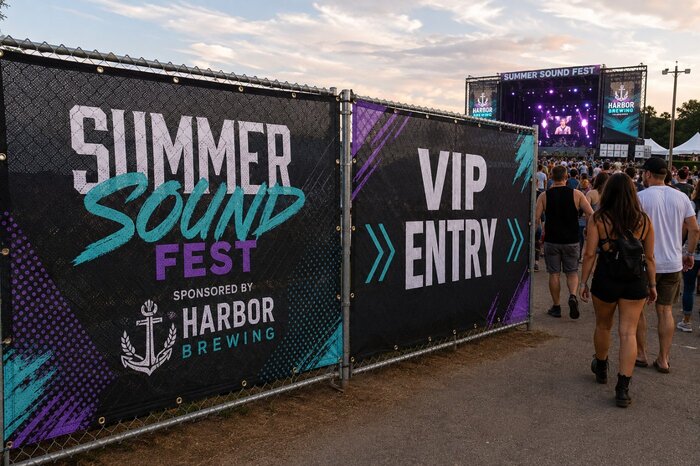 Mesh fence banners displaying concert branding and VIP event entry signs at an outdoor music festival